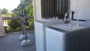 Dos lavadoras blancas sobre un piso de concreto con una baranda metálica y una ventana al fondo.