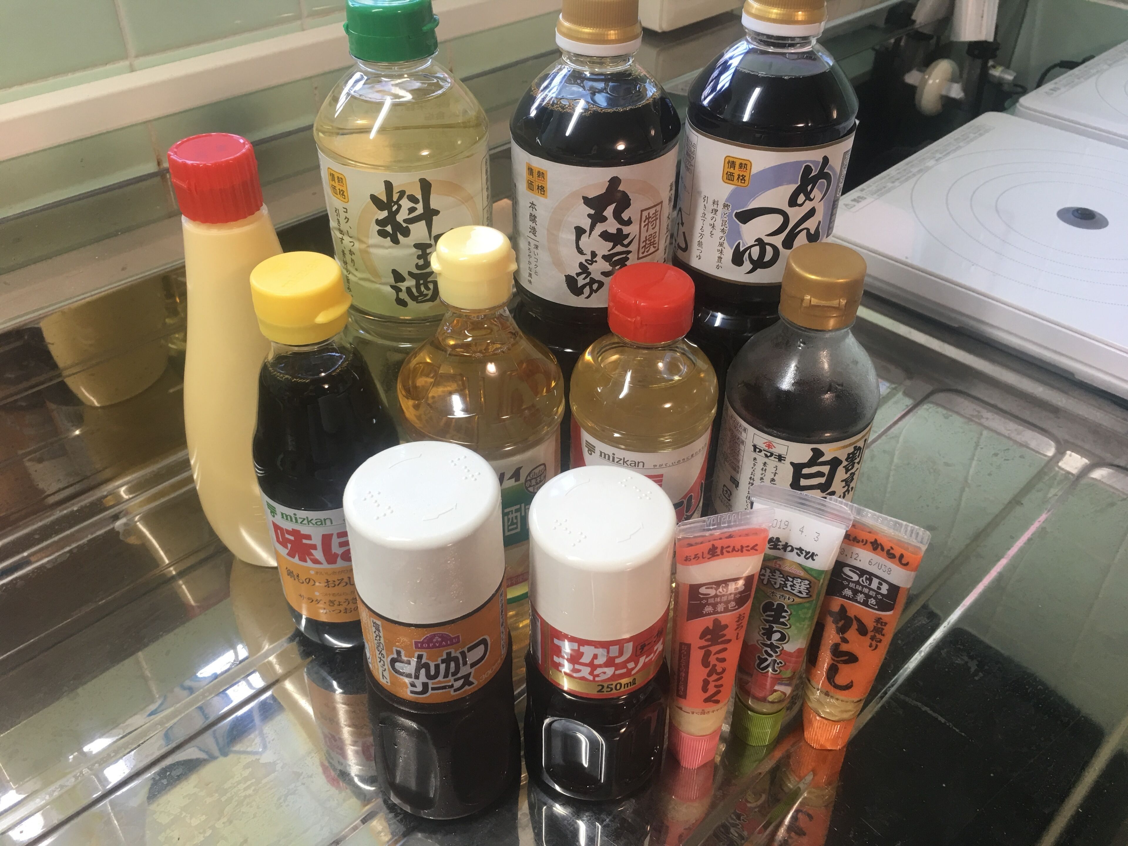 A variety of condiment bottles on a glass counter.