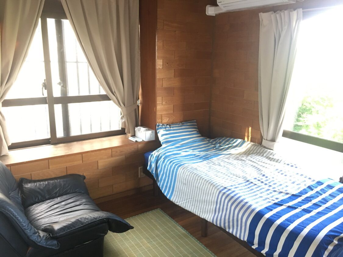 Un dormitorio con una cama, una silla, un ventanal con cortinas y una pared de madera.
