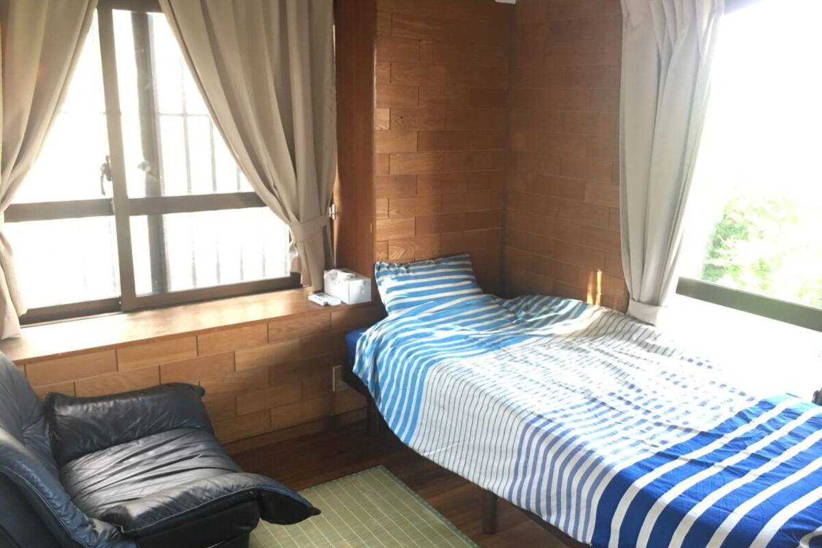 Een slaapkamer met een bed, een stoel, een raam met gordijnen en een houten wand.