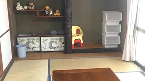 Una habitación con suelo de tatami, una mesa de madera baja, una silla roja, una estantería con peluches y contenedores de almacenamiento.
