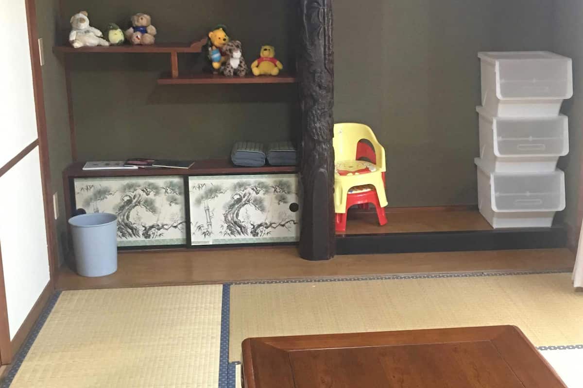 Een kamer met tatami vloerbedekking, een lage houten tafel, een rode stoel, een plank met knuffeldieren en opbergmanden.