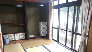 Una habitación con esteras de tatami, un estante de madera, un mueble de almacenamiento y vistas a través de un ventanal grande.