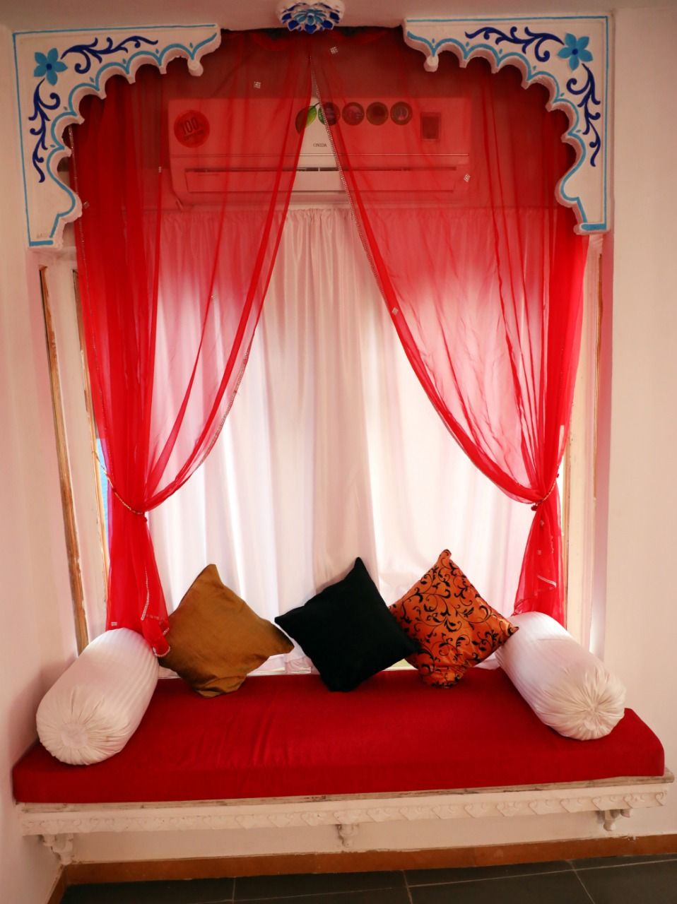 Una ventana con cortinas rojas y un banco con cojines.