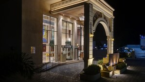 A hotel entrance with a grand archway, large glass windows, and a well-lit facade.