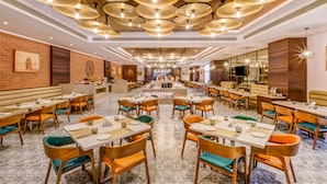 A spacious restaurant with multiple dining tables and chairs, a central bar area, and a patterned floor.