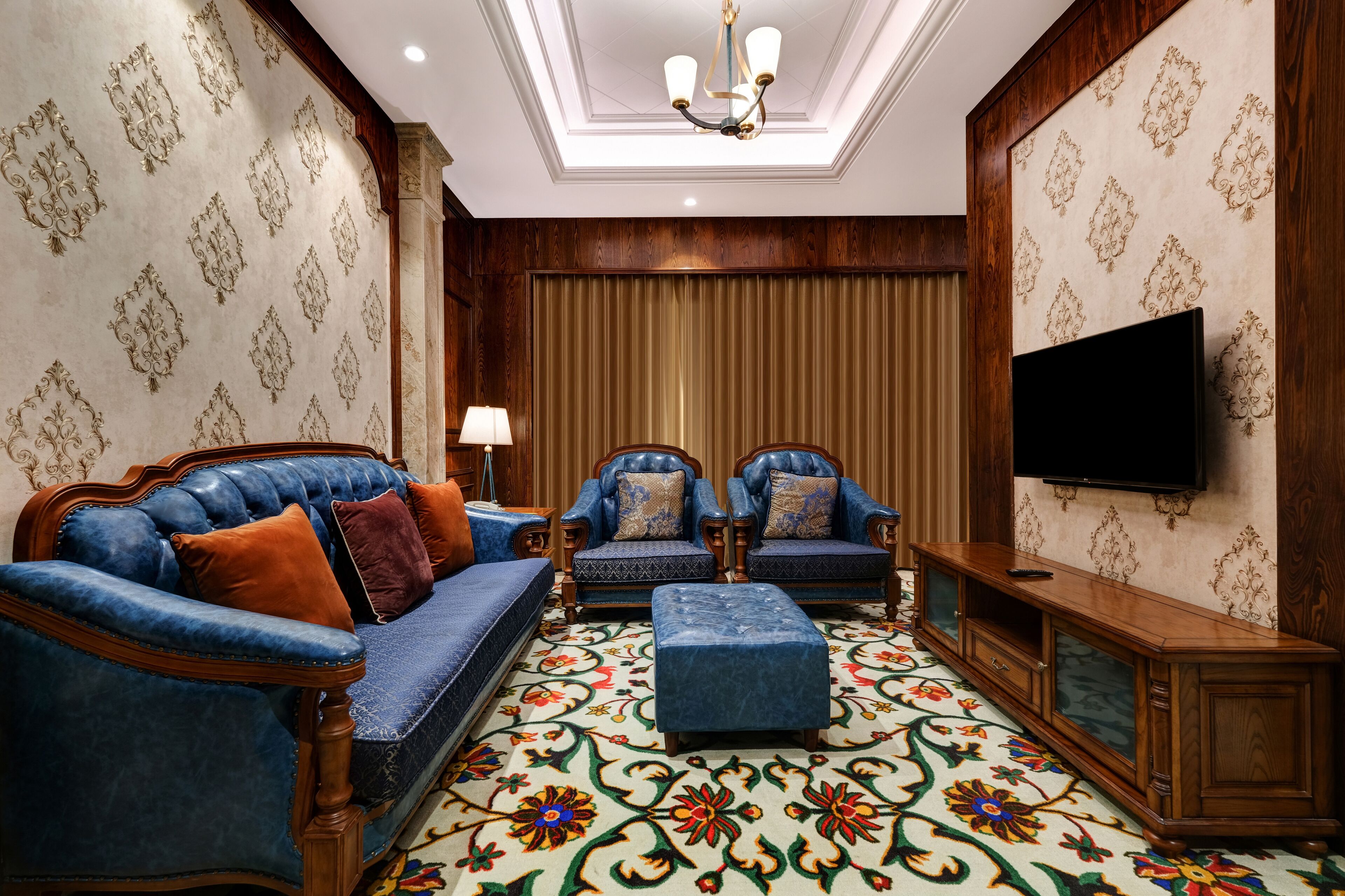 Una sala de estar con un sofá azul, dos sillones, un aparador de madera y un televisor en la pared.