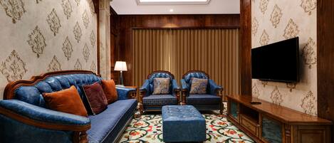 Una sala de estar con un sofá azul, dos sillones, un aparador de madera y un televisor en la pared.