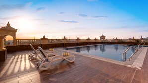 A rooftop pool with sun loungers and a view of the city skyline at sunset.