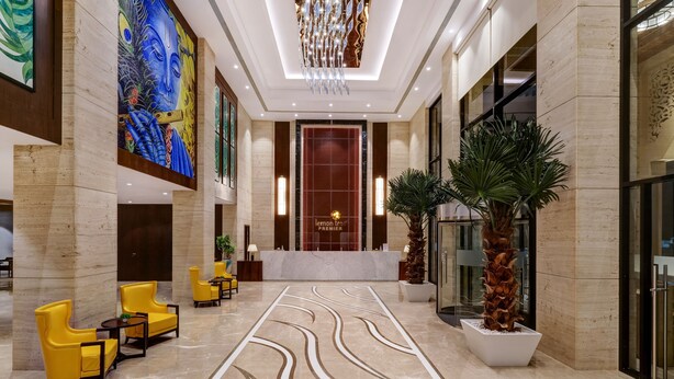 A modern lobby with a reception desk, yellow armchairs, a large mural, and a patterned floor.