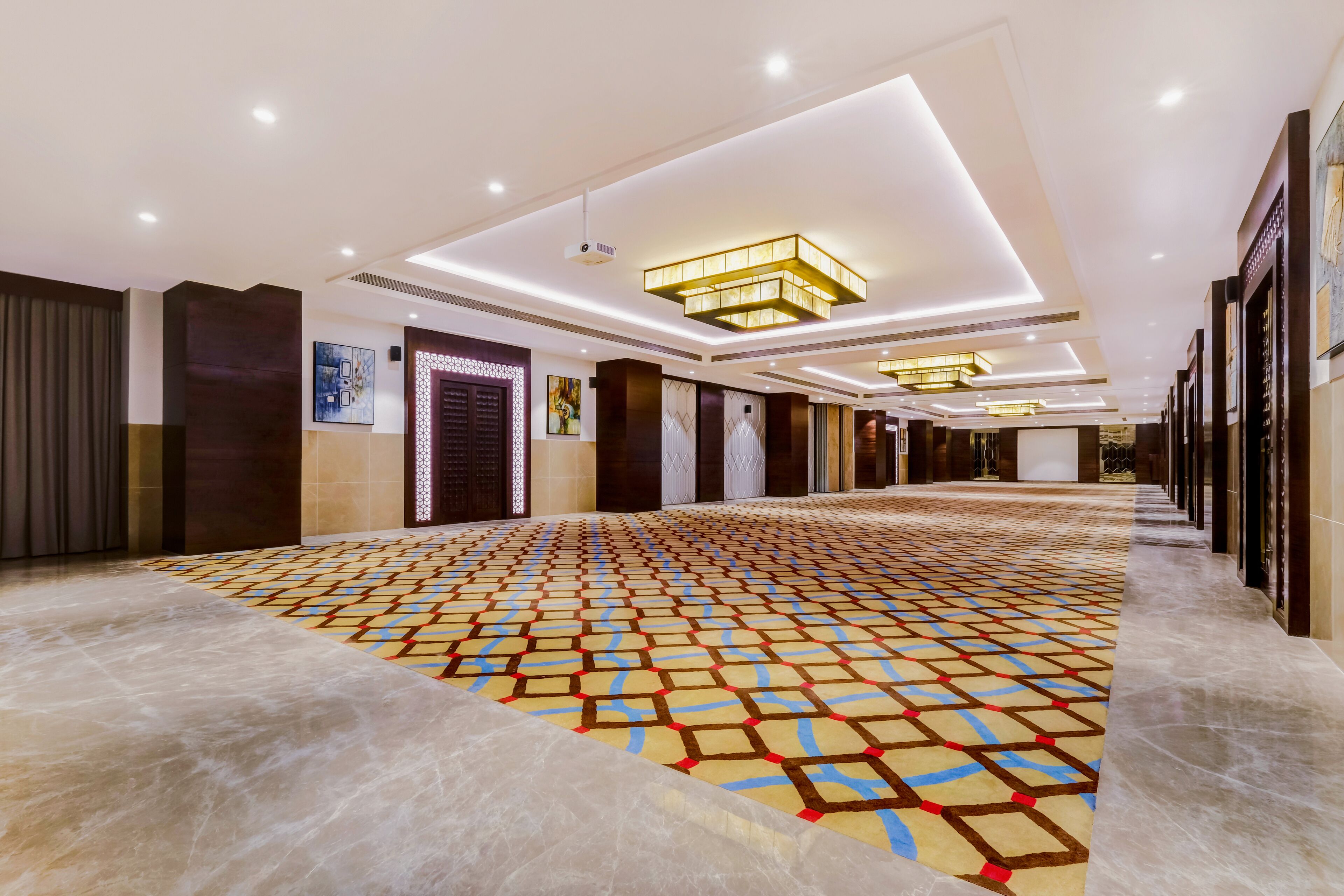 Un pasillo de hotel con alfombra estampada, iluminación empotrada y cuadros en las paredes.