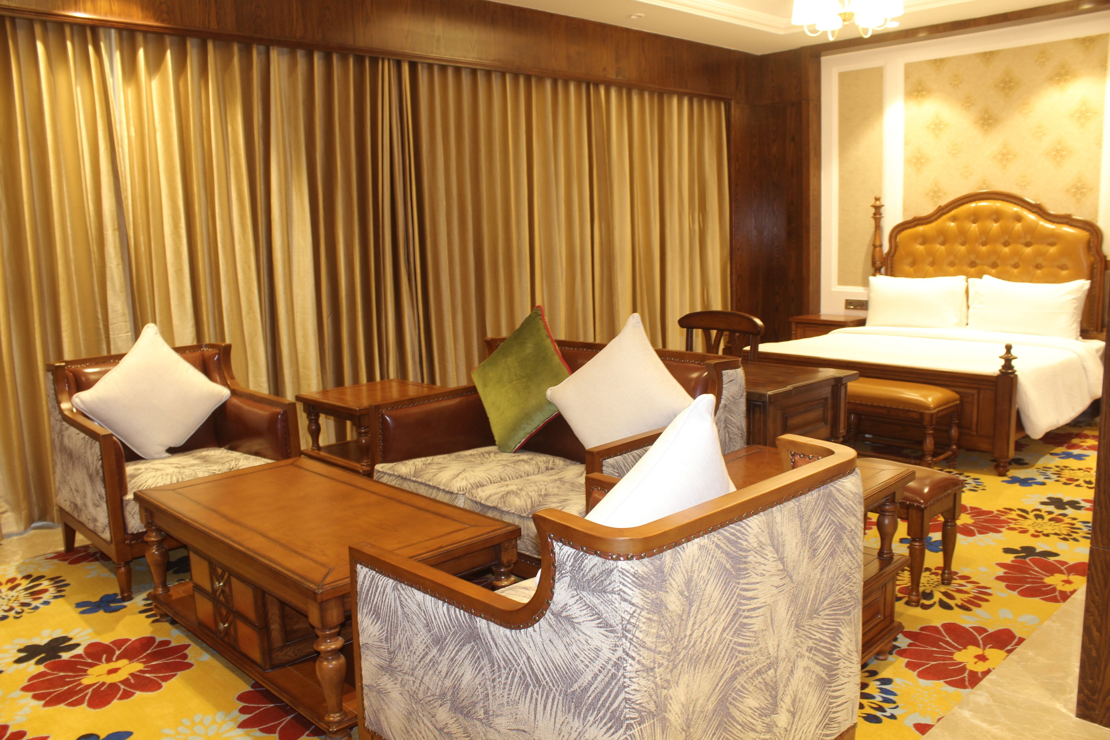 A hotel room with a large bed, a wooden desk, two armchairs, and a sofa.