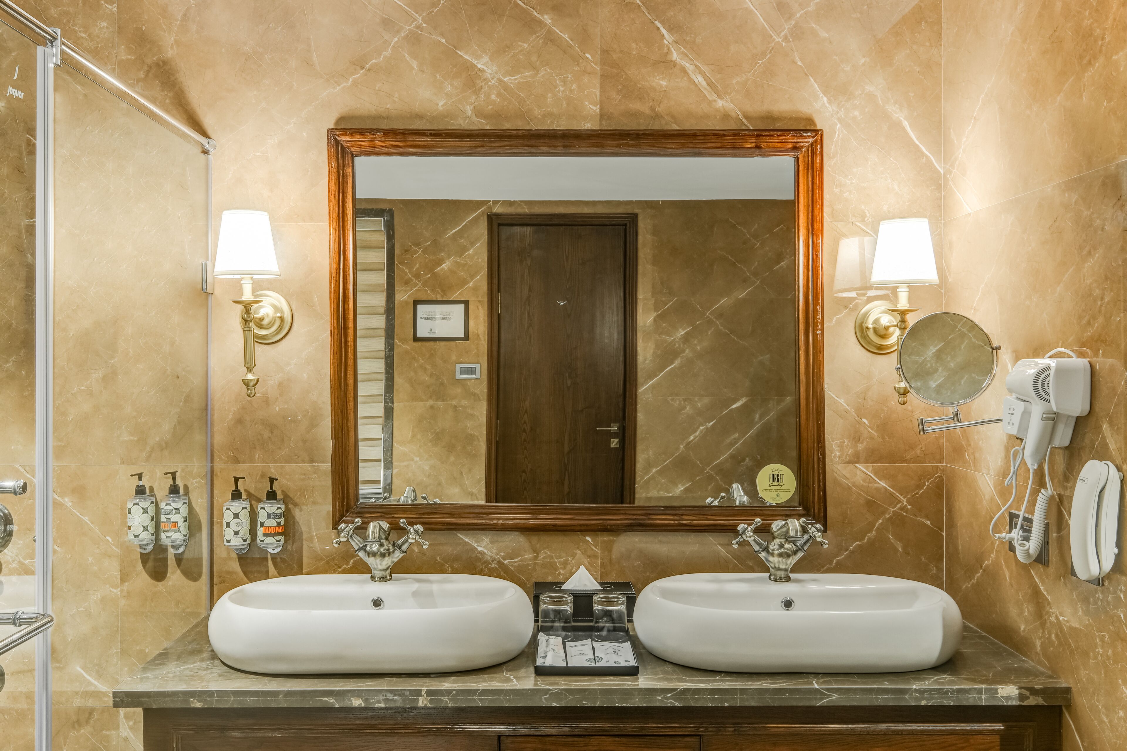 Une salle de bain avec deux lavabos, un grand miroir, des lampes fixées au mur et un sèche-cheveux.
