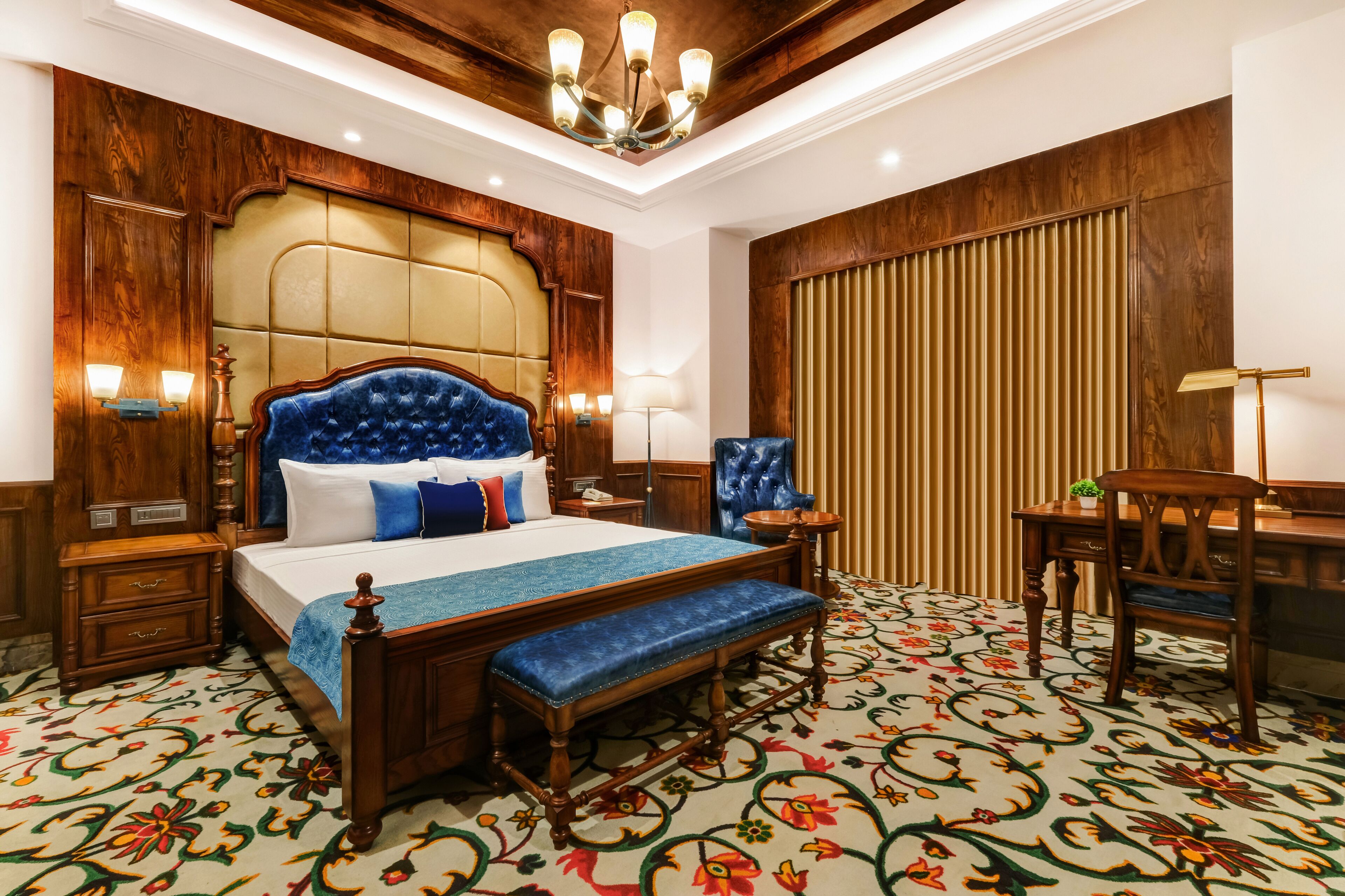 Quarto com cama grande, cabeceira de madeira, mesas de cabeceira, um banco, escrivaninha e cadeira.