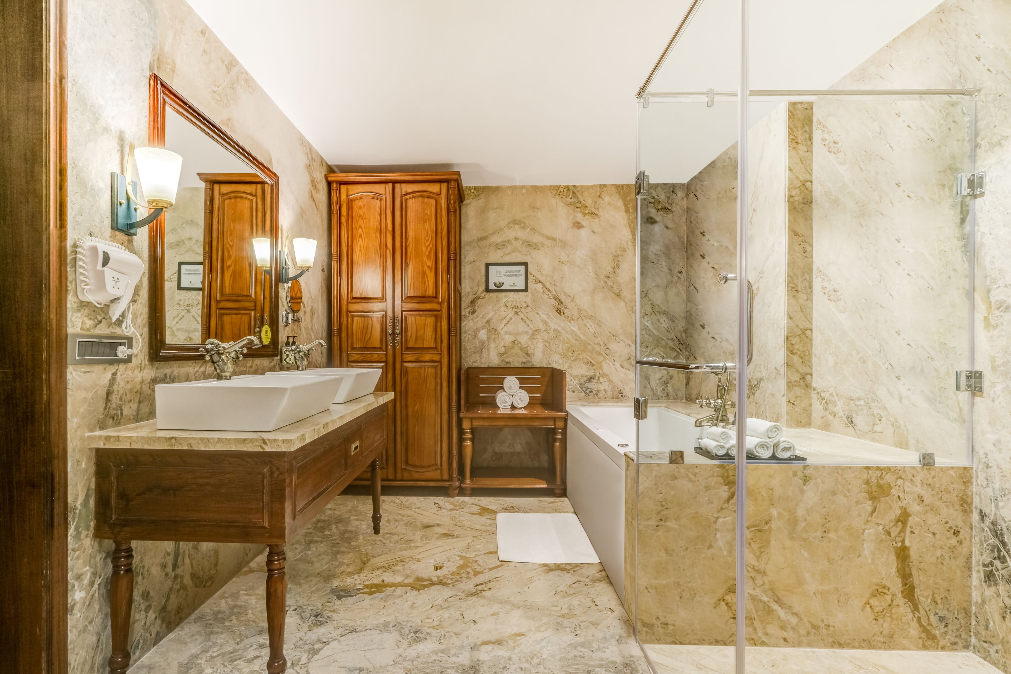 Un baño con dos lavamanos, un mueble de tocador de madera, un espejo grande, cabina de ducha y paredes de mármol.
