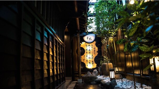 A traditional Japanese garden with a wooden pathway, lanterns, and a sign with Japanese characters. - Hostel Ko-fu (Osaka)