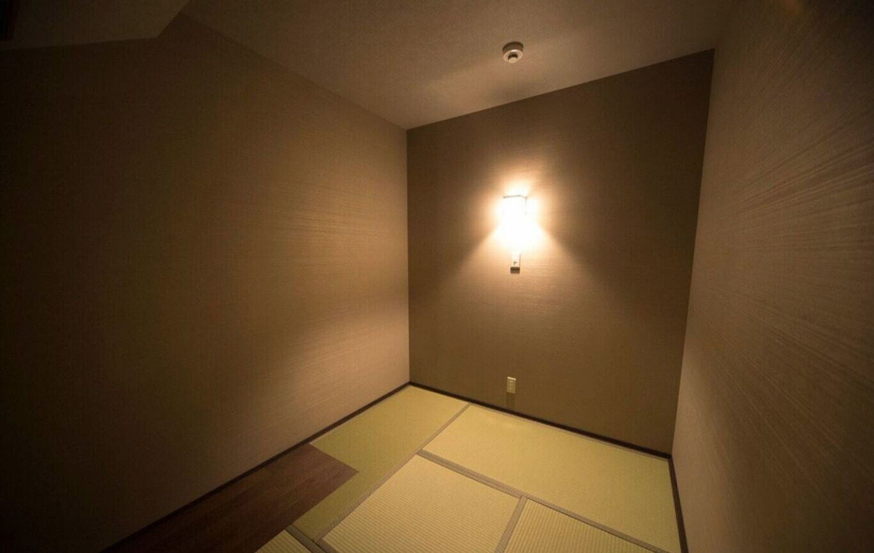 A room with tatami flooring, a wall-mounted light fixture, and a ceiling vent.