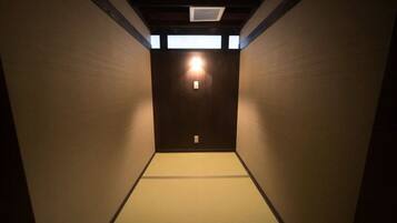 A narrow hallway with tatami mat flooring and a wooden door at the end.