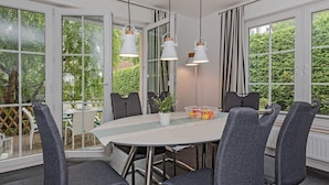 En spiseplads med et rundt bord, seks grå polstrede stole og tre hængende lamper.