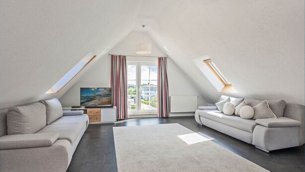 Et moderne loftværelse med et stort ovenlys, en sofa, et fjernsyn og udsigt over byen.