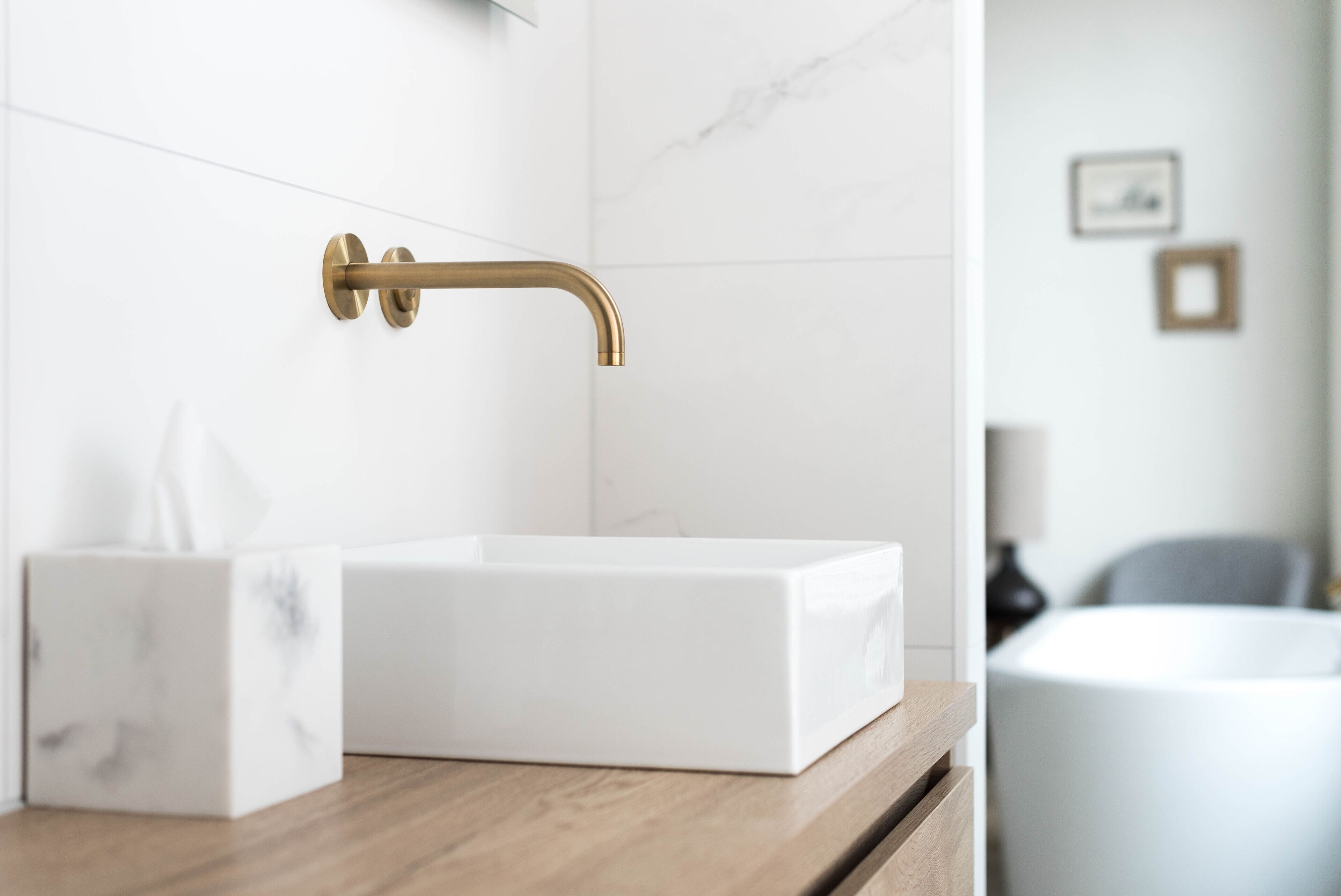 Un baño con lavamanos de mármol blanco, grifo dorado y encimera de madera.
