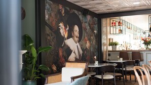 L’intérieur d’un restaurant, avec une fresque murale, des chaises en osier, un bar et un escalier.