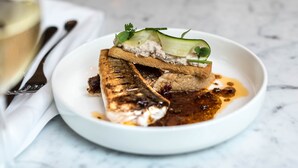 Une assiette blanche avec du poisson grillé, une tranche de pain et une sauce.