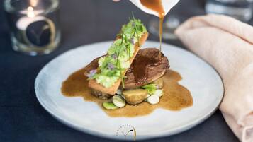 Een bord met een steak, groen bereid en met saus, een kaars en een stoffen servet.