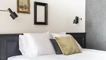 A neatly made bed with white and gray pillows, a black-framed picture frame, and two black wall-mounted lamps.