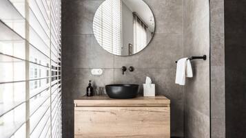 A modern bathroom with a round mirror, wooden vanity, black sink, and towel rack.