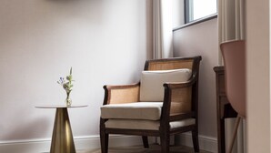 Une pièce d’angle avec une chaise en bois, une petite table ronde ornée d’un vase et une fenêtre.
