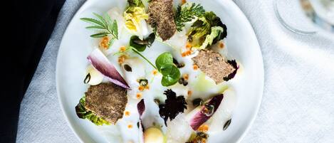 Un plato blanco con diversos alimentos, incluyendo verduras, un trozo de carne y una cucharada de salsa.
