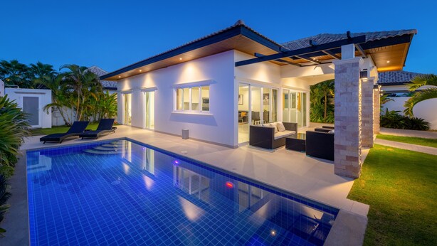 Een modern huis met een zwembad, buitenmeubilair en een goed verlicht terras.