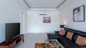 Een moderne woonkamer met een flatscreen televisie, een zwarte leren bank, een glazen salontafel en een kamerkleed met een patroon.