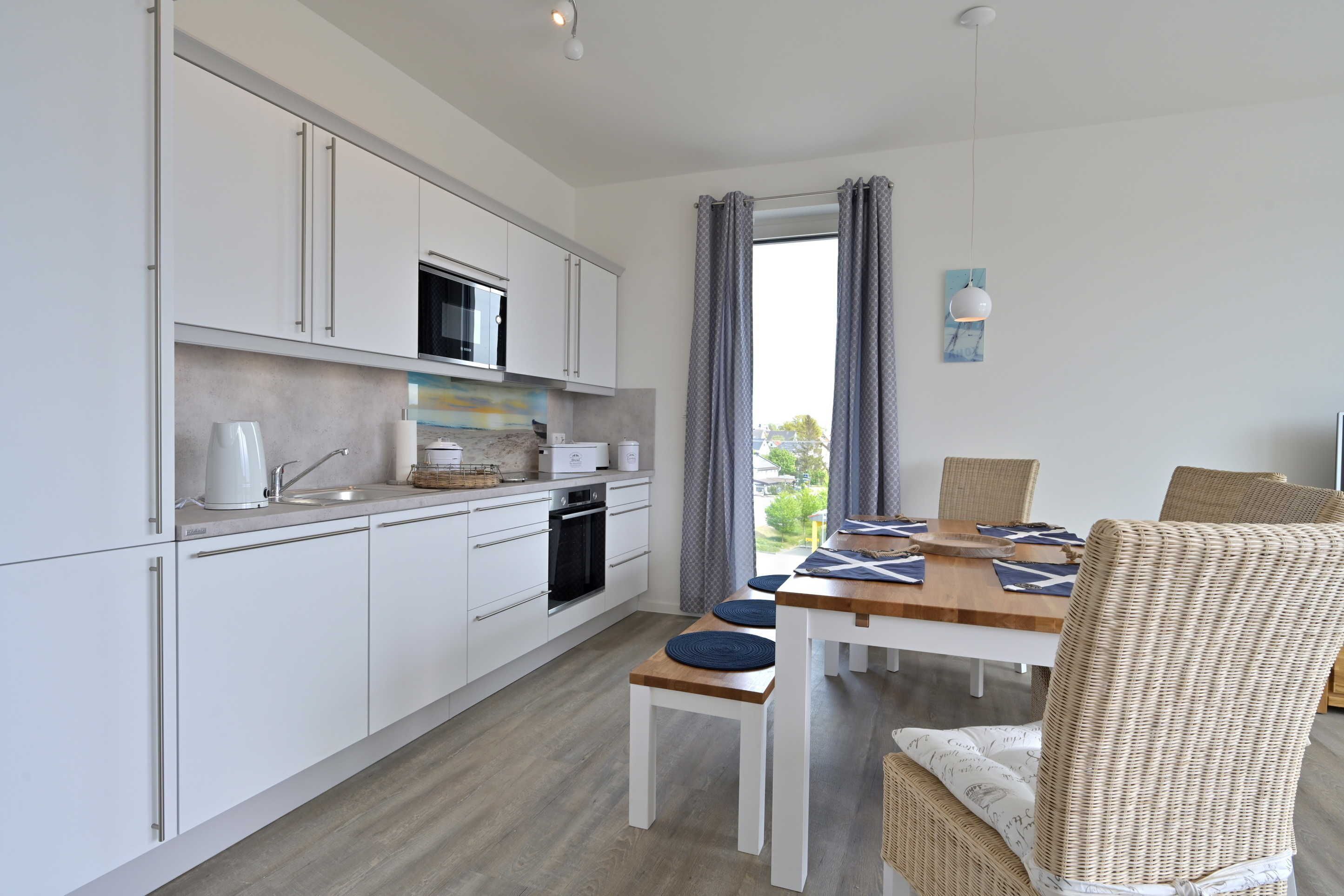 A modern kitchen with white cabinets, a microwave, and a dining area with wicker chairs and a wooden table.