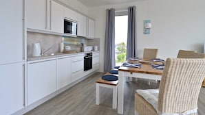 A modern kitchen with white cabinets, a microwave, and a dining area with wicker chairs and a wooden table.