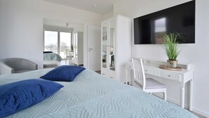 A modern bedroom with a large bed, a desk, a chair, and a TV on the wall.