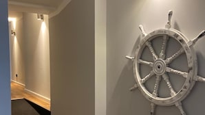 A hallway with a wooden floor, a grey wall, and a ship's wheel decoration. - City Maritim Rooms (Bremerhaven)