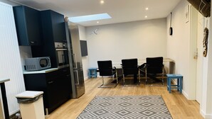 A modern kitchen with dark cabinets, a stainless steel refrigerator, and a microwave. There is a patterned rug on the floor and a small blue stool. - City Maritim Rooms (Bremerhaven)