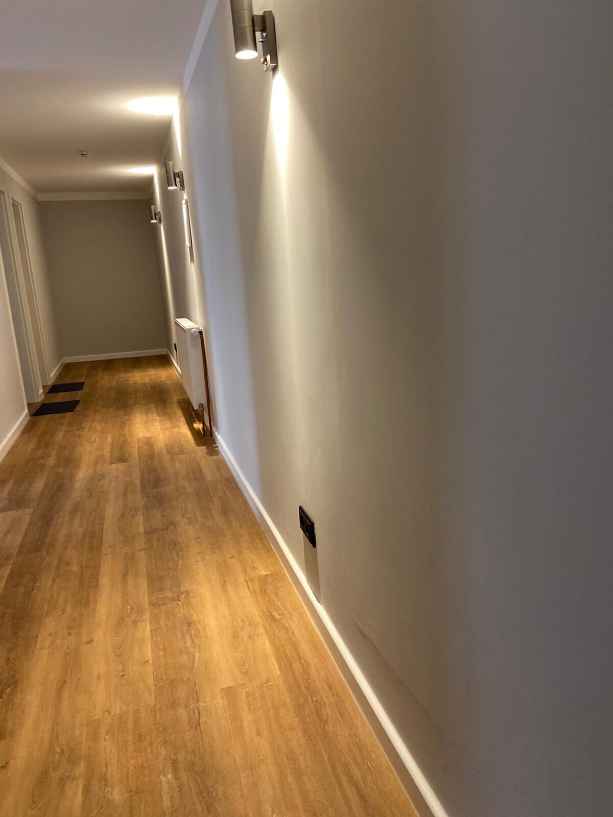 A hallway with wooden flooring, white walls, and recessed lighting.