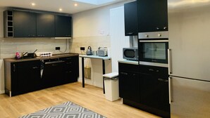 A modern kitchen with black cabinets, a built-in oven, a microwave, and a stainless steel refrigerator. - City Maritim Rooms (Bremerhaven)
