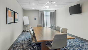 A conference room with a long table, six chairs, a whiteboard, and a TV on the wall.