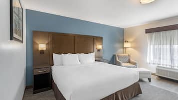 Una habitación de hotel con una cama grande, mesitas de noche, una silla, un ventanal con cortinas y lámparas fijadas a la pared.