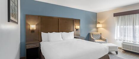 A hotel room with a large bed, bedside tables, a chair, a window with curtains, and wall-mounted lamps.