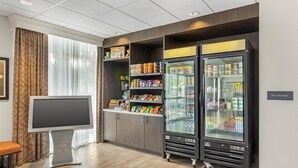 Une chambre d’hôtel dotée d’un grand téléviseur à écran plat, d’une kitchenette avec des étagères remplies de collations et de boissons, et de deux réfrigérateurs de grande taille.