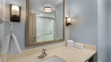 A bathroom with a large mirror, a sink, a towel rack, and a shower visible through the glass door.
