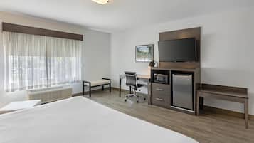 Quarto de hotel com cama grande, escrivaninha com cadeira, televisão, micro-ondas e um banco.