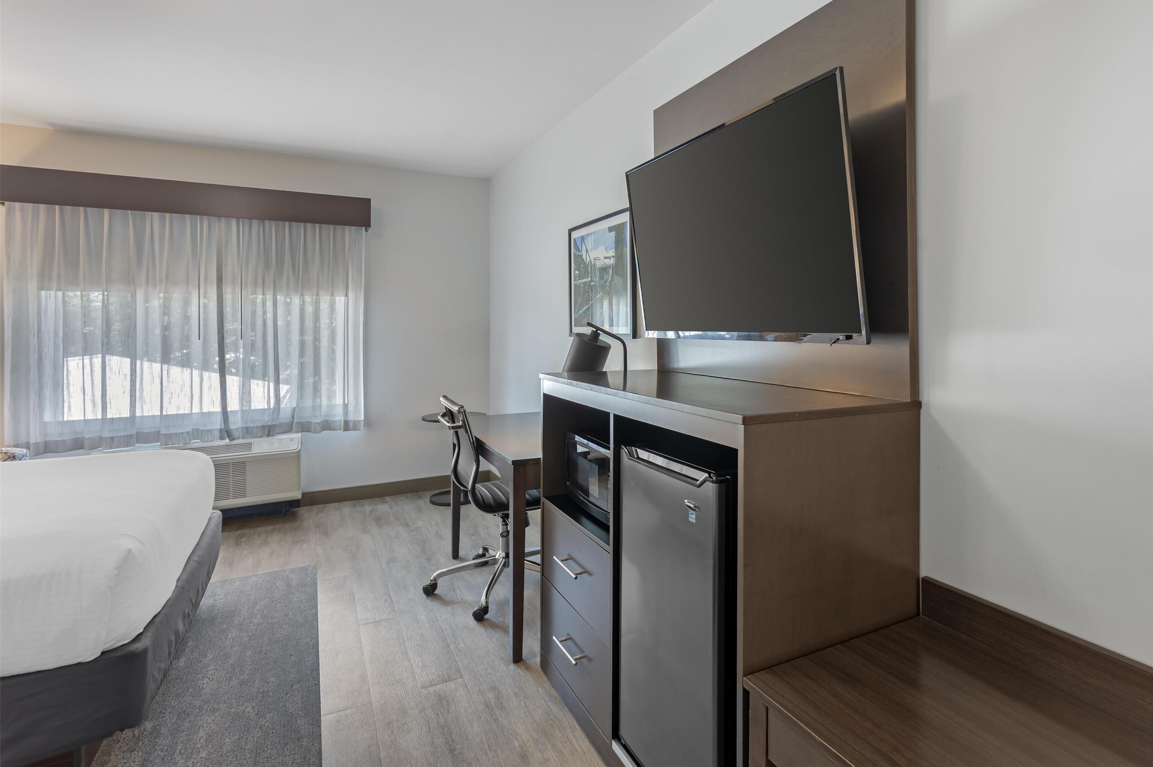 Quarto de hotel moderno com cama, escrivaninha, televisão de tela plana, frigorífico e uma cadeira.