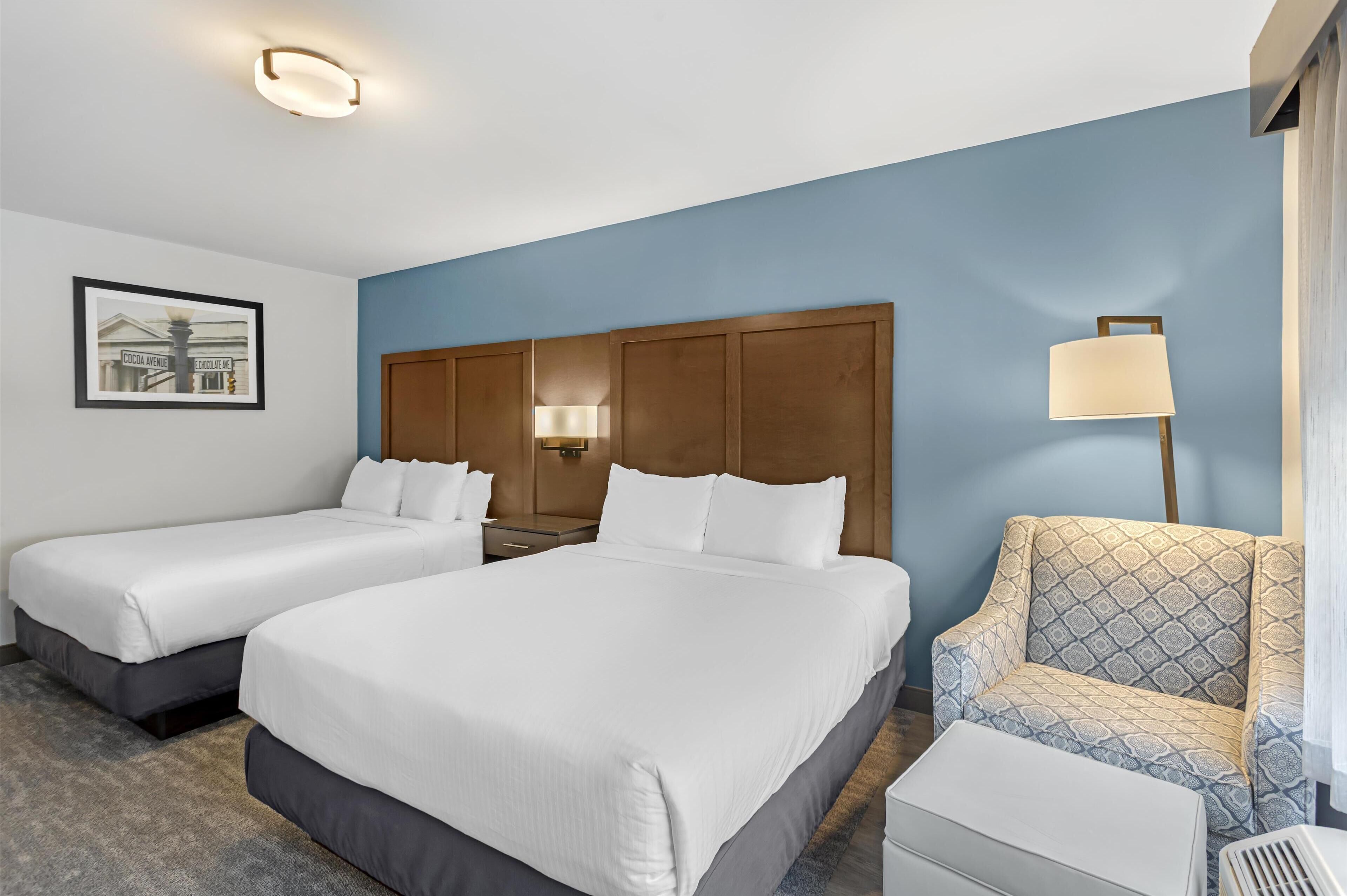Een hotelkamer met twee bedden, een houten hoofdbord, een nachtkastje met een lamp, een gestreept fauteuil en een kleine tafel.