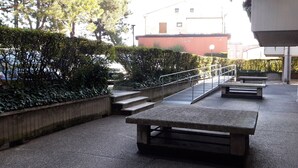 A paved outdoor area with steps leading to a building, surrounded by greenery and a metal railing. - Appartamento San Massimo (Verona)